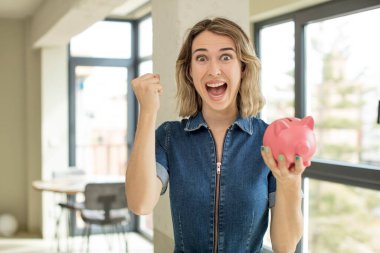 Güzel kadın şokta, gülüyor ve başarıyı kutluyor. Domuz kumbarası konsepti