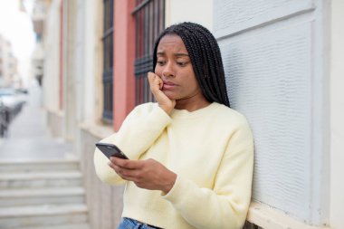 Siyah afro kadın korkmuş, endişeli ya da kızgın hissediyor ve yan tarafa bakıyor. akıllı telefon konseptini kullanarak