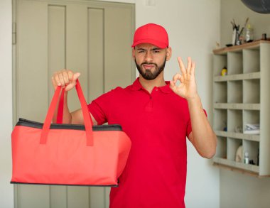 Genç yetişkin bir adam kendini mutlu hissediyor. Onayını iyi bir jestle gösteriyor. Pizza teslimatçısı konsepti