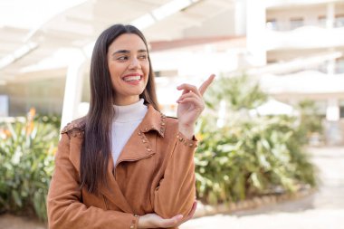 pretty young adult woman smiling happily and looking sideways, wondering, thinking or having an idea