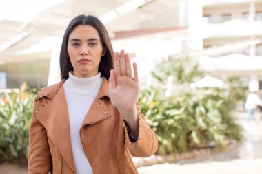 pretty young adult woman looking serious, stern, displeased and angry showing open palm making stop gesture