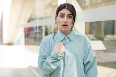 Şok olmuş ve ağzı açık, kendini işaret eden güzel bir kadın.