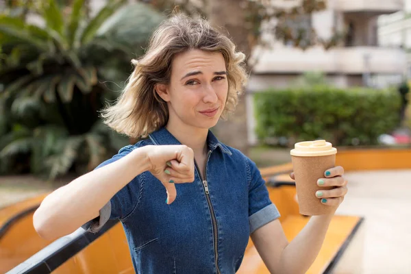 stock image pretty woman feeling cross,showing thumbs down. take away coffee concept