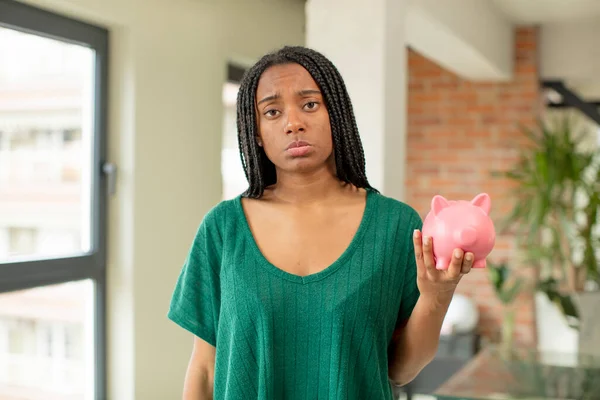 black afro woman feeling sad and whiney with an unhappy look and crying. piggy bank concept