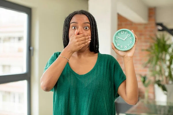 黒いアフロの女が手で口を覆いショックや驚きの表情で 目覚まし時計のコンセプト — ストック写真