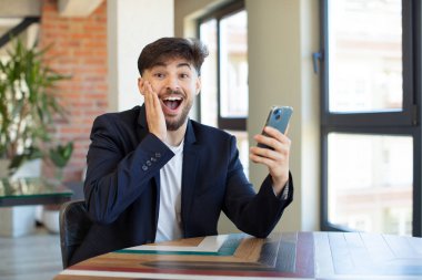 Genç yakışıklı adam kendini mutlu hissediyor ve inanılmaz bir şeye hayret ediyor. akıllı telefon kavramı