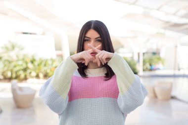 Genç ve güzel bir kadın ciddi ve hoşnutsuz görünüyor. İki parmağın önde olsun, reddedilmek için, sessizlik istiyor.