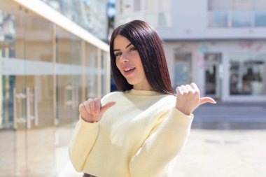 Genç ve güzel bir kadın neşeyle gülümsüyor ve yan taraftaki fotokopi alanını işaret ediyor, mutlu ve tatmin olmuş hissediyor.