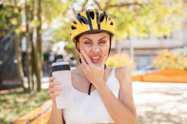 Ağzı ve gözleri açık, eli çenesinde genç ve güzel bir kadın. bisiklet kaskı konsepti