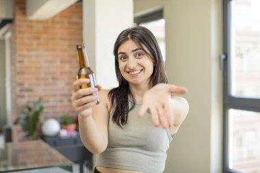 Genç bir kadın mutlu bir şekilde gülümser ve bir konsept sunar ya da gösterir. bira şişesi