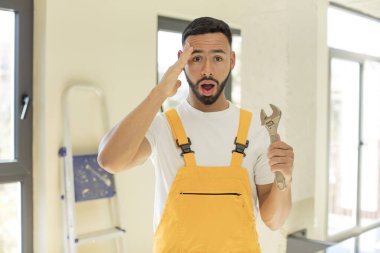 Arap yakışıklı Arap adam mutlu, şaşkın ve şaşırmış görünüyor. İngiliz anahtarı olan bir tamirci.