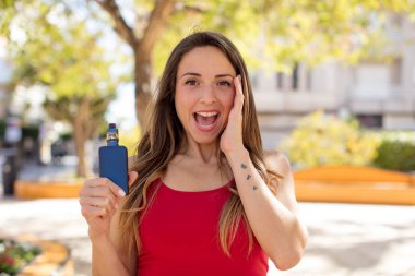 Güzel bir kadın kendini mutlu hissediyor ve inanılmaz bir şeye hayret ediyor. vaper konsepti