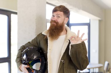 red hair man feeling happy, showing approval with okay gesture with a motorbike helmet clipart