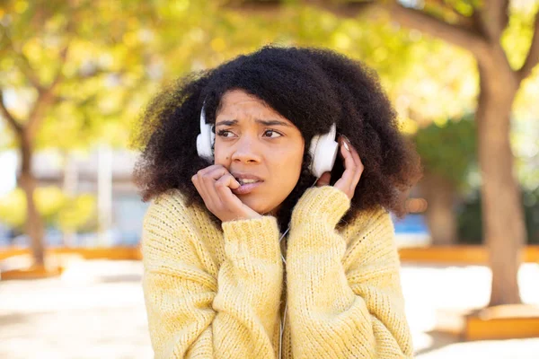 pretty afro black woman feeling scared, worried or angry and looking to the side. listening music with headphones