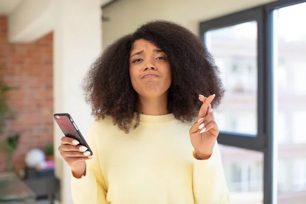 かなりアフロ黒人女性が指を渡って幸運を願ってる スマートフォンのコンセプト — ストック写真