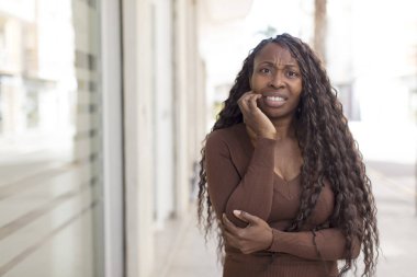 Afro güzel siyah kadın şok ve inançsızlık içinde ağzı açık, elleri yanağında ve kolları çapraz, sersemlemiş ve şaşırmış hissediyor