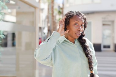 Afro güzel siyah kadın mutlu görünüyor, dinliyor, gizli bir konuşma veya dedikodu duymaya çalışıyor, kulak misafiri oluyor.