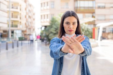 pretty young adult woman covering face with hand and putting other hand up front to stop camera, refusing photos or pictures