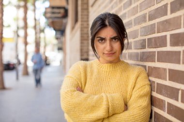 Güzel bir kadın hayal kırıklığına uğramış, hayal kırıklığına uğramış, ciddi görünüyor, kızgın ve kollarını kavuşturmuş.