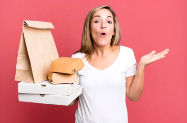 Güzel sarışın kadın şaşırmış ve şok olmuş görünüyor. Çenesi düşmüş ve elinde bir nesne var. Teslimat yiyecek paketleri kavramını kaldırır