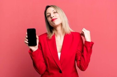 Güzel sarışın kadın kibirli, başarılı, pozitif ve gururlu görünüyor. İş kadını telefon ekranı gösteriyor