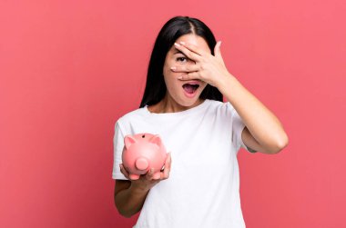 İspanyol görünümlü güzel bir kadın şok olmuş, korkmuş ya da korkmuş, yüzlerini domuz kumbarasıyla kapatmış.