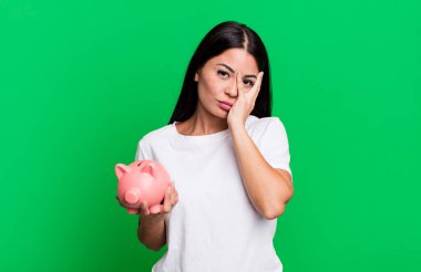 hispanic pretty woman feeling bored, frustrated and sleepy after a tiresome with a piggy bank