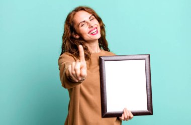 hispanic pretty woman smiling proudly and confidently making number one with an empty blank frame