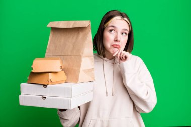 Genç, güzel bir kadın düşünüyor, kuşkulu ve şaşkın hissediyor. Fast food konseptini kaldır.