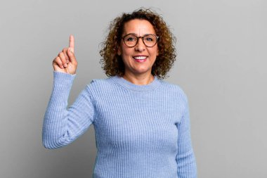 Orta yaşlı İspanyol kadın neşeli ve mutlu bir şekilde gülümsüyor, tek eliyle boşluğu dolduruyor.