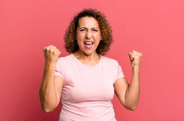 Orta yaşlı İspanyol kadın mutlu, pozitif ve başarılı hissediyor, zaferi, başarıları veya iyi şansı kutluyor.