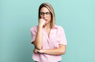 blonde adult woman feeling serious, thoughtful and concerned, staring sideways with hand pressed against chin