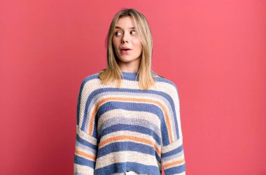 Sarışın, güzel bir kadın şaşkın, mutlu, şaşkın ve şaşırmış hissediyor, ağzı açık bir şekilde yana bakıyor.