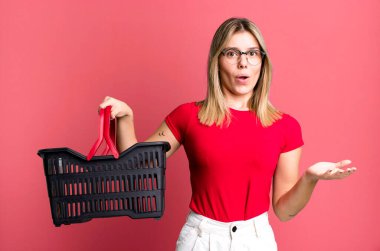 young pretty woman feeling extremely shocked and surprised. empty shopping basket concept