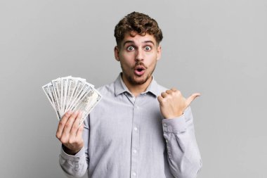 Kafkasyalı genç bir adam inançsızlıktan şaşkın şaşkın bakıyor. Dolar banknotları konsepti