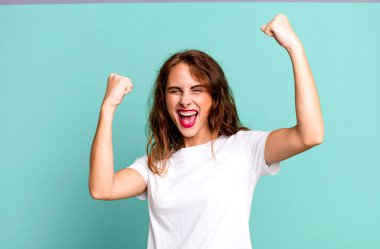 Genç ve güzel bir kadın muzaffer bir şekilde bağırıyor. Heyecanlı, mutlu ve şaşırmış görünüyor. Kutlama yapıyor.