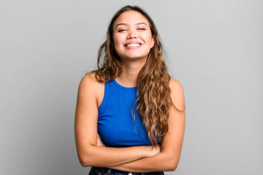 Genç, güzel bir kadın mutlu, gururlu ve tatmin olmuş görünüyor. Kollarını kavuşturup gülümsüyor.