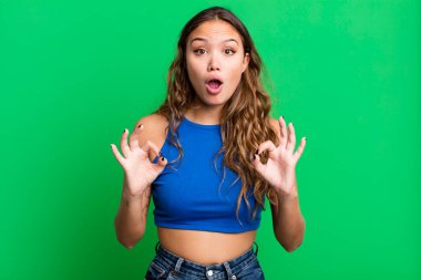 Genç, güzel bir kadın şok olmuş, şaşırmış ve şaşırmış hissediyor. İki eliyle de onay işareti yapıyor.