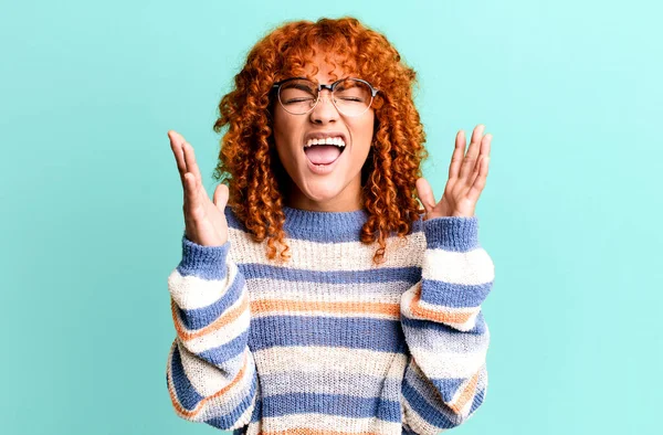 stock image redhair pretty woman furiously screaming, feeling stressed and annoyed with hands up in the air saying why me