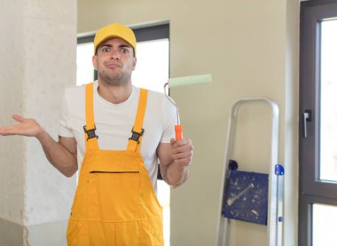 Genç yakışıklı adam omuz silkiyor, kafası karışık ve kararsız. resim ev kavramı