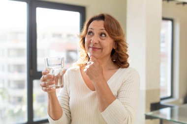 Orta yaşlı güzel bir kadın mutlu, kendinden emin ve elleri çenesinde gülümsüyor. su bardağı