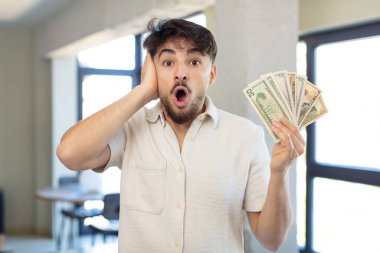Genç ve yakışıklı bir adam şok olmuş ve şaşırmış hissediyor. Dolar banknotları konsepti