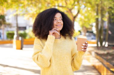 Güzel, afro siyah bir kadın mutlu, kendinden emin, elleri çenesinde gülümsüyor. kahve konseptini kaldır.