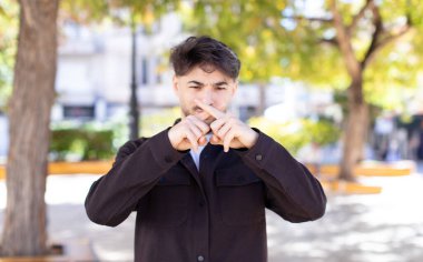 Genç ve yakışıklı bir adam ciddi ve hoşnutsuz görünüyor. İki parmağın önde olsun, reddedilsin ve sessizlik istesin.