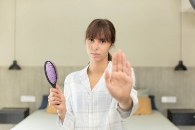 Genç ve güzel bir kadın ciddi görünüyor. Avuç içini gösteriyor. Durdurma hareketi yapıyor. saç tarağı konsepti