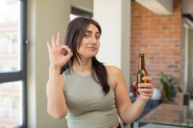 Genç bir kadın kendini mutlu hissediyor. Onayını iyi bir jestle gösteriyor. bira şişesi