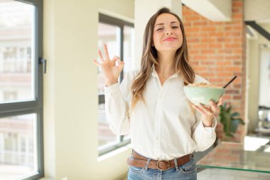 Güzel bir kadın kendini mutlu hissediyor, iyi bir jestle onaylıyor. Kahvaltı kasesi konsepti