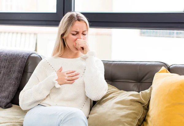 stock image young pretty woman feeling ill with a sore throat and flu symptoms, coughing with mouth covered sitting on a couch