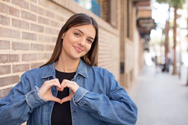Genç ve güzel bir kadın gülümsüyor ve mutlu, sevimli, romantik ve aşık, iki eliyle kalbi şekillendiriyor