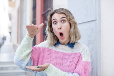 Güzel bir kadın şaşkın bir ifadeyle gülümsüyor ve elinde bir şey tutuyor.